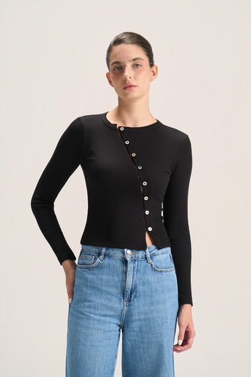 A model wearing a black long-sleeve knit top with a decorative button-down front and light blue jeans, photographed against a plain light gray studio background.