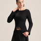 A model wearing a black long-sleeve boat-neck top with a unique asymmetrical hem and black wide-leg trousers, posed against a solid light beige background.
