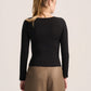 A woman shown from the back wearing a fitted black long-sleeve top and tan wide-leg pants against a plain light background.