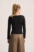 A woman shown from the back wearing a fitted black long-sleeve top and tan wide-leg pants against a plain light background.