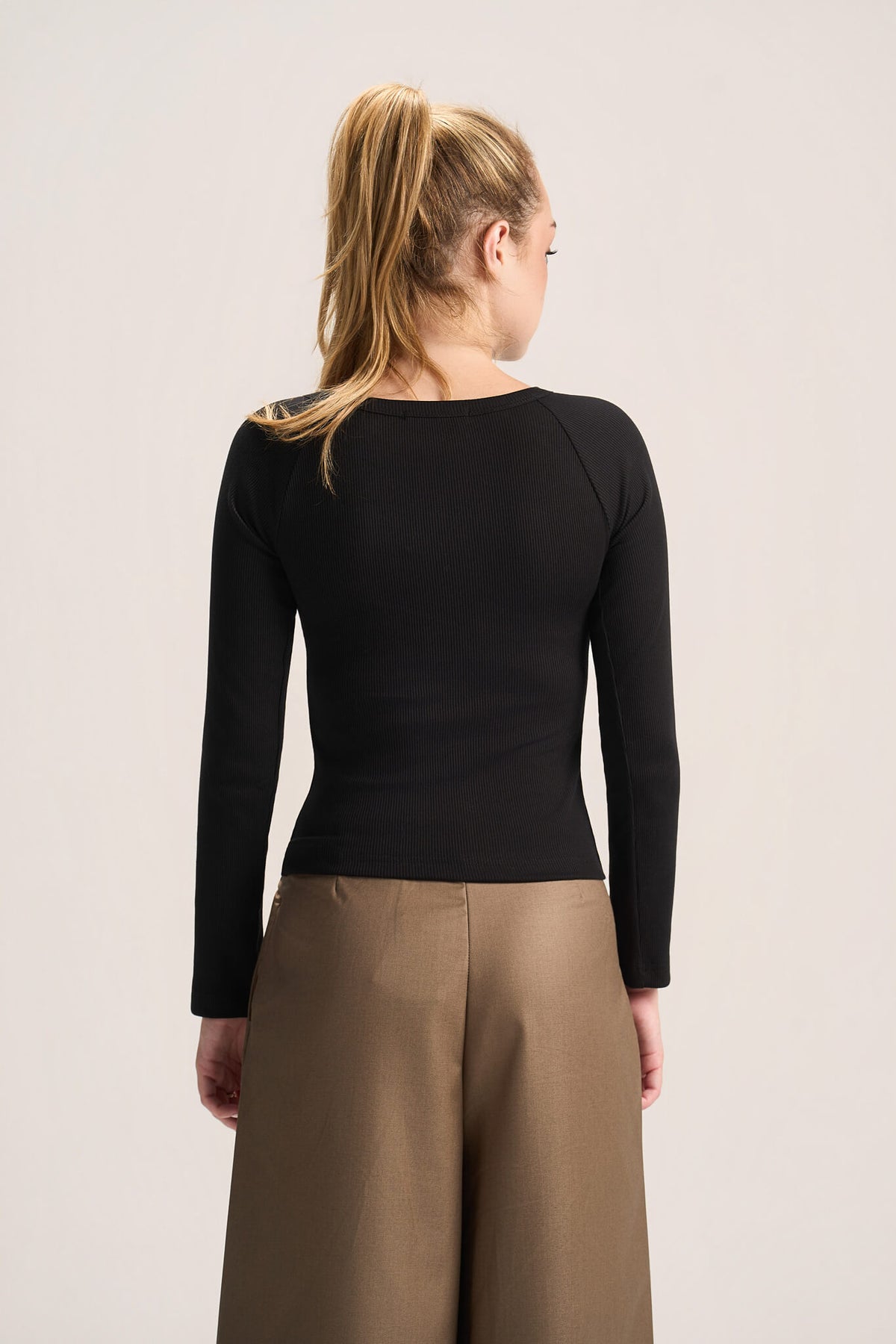 A woman shown from the back wearing a fitted black long-sleeve top and tan wide-leg pants against a plain light background.