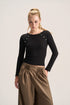 A woman modeling a fitted black long-sleeve top with decorative silver-tone studs along the shoulders, paired with brown pleated wide-leg pants, against a plain light gray studio background.