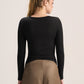 A woman shown from the back wearing a fitted black long-sleeve top and tan wide-leg pants against a plain light background.
