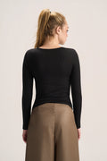 A woman shown from the back wearing a fitted black long-sleeve top and tan wide-leg pants against a plain light background.