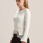 A woman modeling a fitted long-sleeve cream knit top with a sheer lace hem, paired with dark brown wide-leg pants, against a plain light beige studio background.