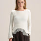 A woman modeling a cream long-sleeve knit top with a silver lace hem detail, paired with dark brown wide-leg trousers, against a solid light beige studio background.