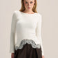 A woman modeling a white long-sleeve knit top with a scalloped silver lace hem, paired with a dark brown skirt, against a plain light beige studio background.