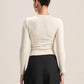 A woman shown from the back wearing a fitted long-sleeve cream top and black wide-leg pants against a plain light beige studio background.