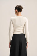 A woman shown from the back wearing a fitted long-sleeve cream top and black wide-leg pants against a plain light beige studio background.