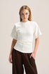 A woman modeling a short-sleeve white mock-neck top with a unique gathered waist, paired with dark brown wide-leg pants, against a solid light beige background.