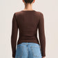 A woman viewed from the back wearing a fitted brown long-sleeve top and light blue jeans against a plain light background.