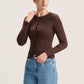 A woman modeling a fitted, long-sleeve brown button-front top paired with light blue jeans, standing against a plain light beige studio background.