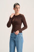 A woman modeling a fitted, long-sleeve brown button-front top paired with light blue jeans, standing against a plain light beige studio background.