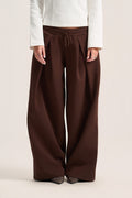 A person wearing wide-leg brown drawstring pants with a white long-sleeve top, shown from the chest down against a plain light beige studio background.