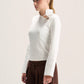 A woman wearing a fitted white long-sleeve mock-neck top with a decorative collar and dark brown wide-leg pants, photographed against a plain light background.