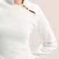 A close-up of a model wearing a white long-sleeve top with a mock neck and decorative cutout details on the chest, paired with brown bottoms against a light beige background.