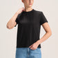 A woman modeling a black short-sleeve crewneck t-shirt paired with light blue jeans, standing against a plain light beige studio background.