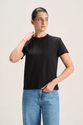 A woman modeling a black short-sleeve crewneck t-shirt paired with light blue jeans, standing against a plain light beige studio background.
