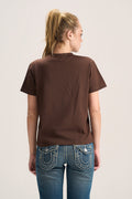 A woman viewed from the back wearing a plain brown short-sleeve t-shirt and blue jeans with contrast stitching, set against a light gray studio background.