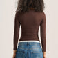 A person shown from the back wearing a fitted long-sleeve ribbed top in dark brown and blue jeans, against a plain light background.