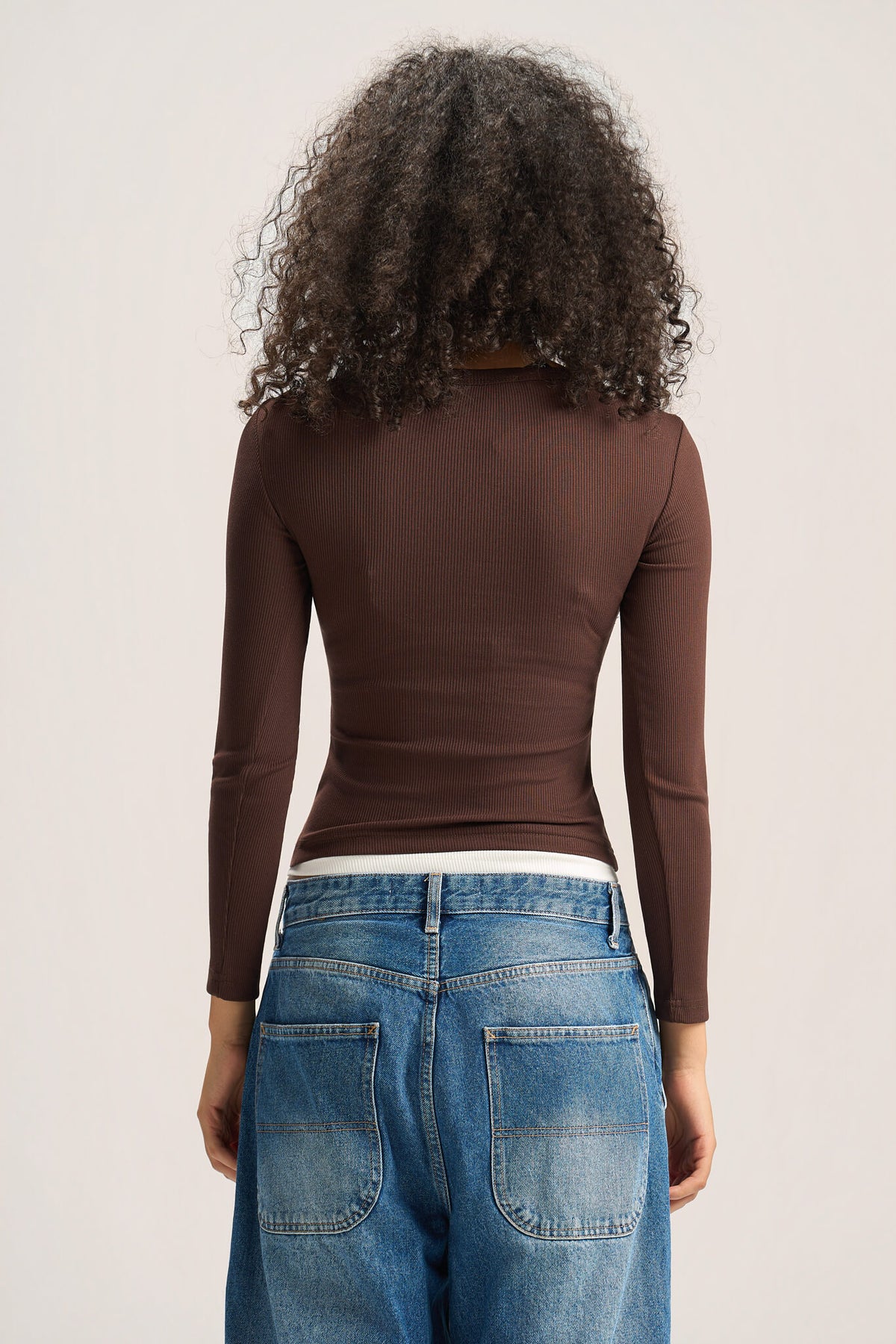 A person shown from the back wearing a fitted long-sleeve ribbed top in dark brown and blue jeans, against a plain light background.