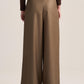 A model shown from the back wearing high-waisted, wide-leg trousers in a warm taupe-brown color, paired with a dark brown long-sleeve top and black shoes, against a solid light beige studio background.