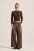 A model stands against a plain beige studio background wearing a dark brown ribbed long-sleeve wrap-style top with decorative buttons and high-waisted olive brown wide-leg trousers.