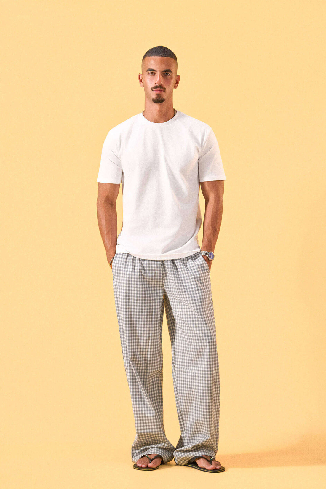 a man wearing a white tee and grey and white checkered lounge pants