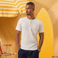 a male wearing  an off white t-shirt with buttons at the top that is a ribbed material 