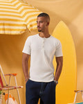 a male wearing  an off white t-shirt with buttons at the top that is a ribbed material 