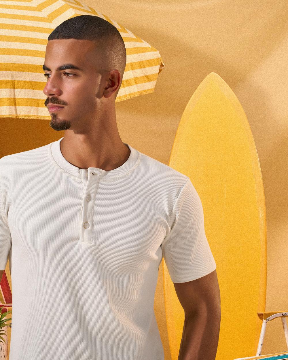 a male wearing  an off white t-shirt with buttons at the top that is a ribbed material 