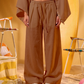 Person wearing a brown outfit with wide-leg pants against a yellow background