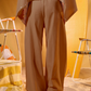 Person wearing a beige outfit with wide-leg pants and a matching top against a yellow background.