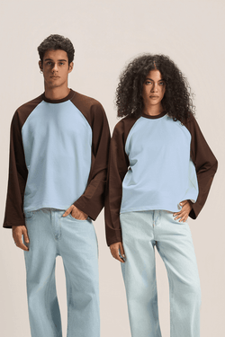 Two models wearing matching brown and sky blue raglan long-sleeve shirts and light blue jeans, standing against a neutral beige studio background.