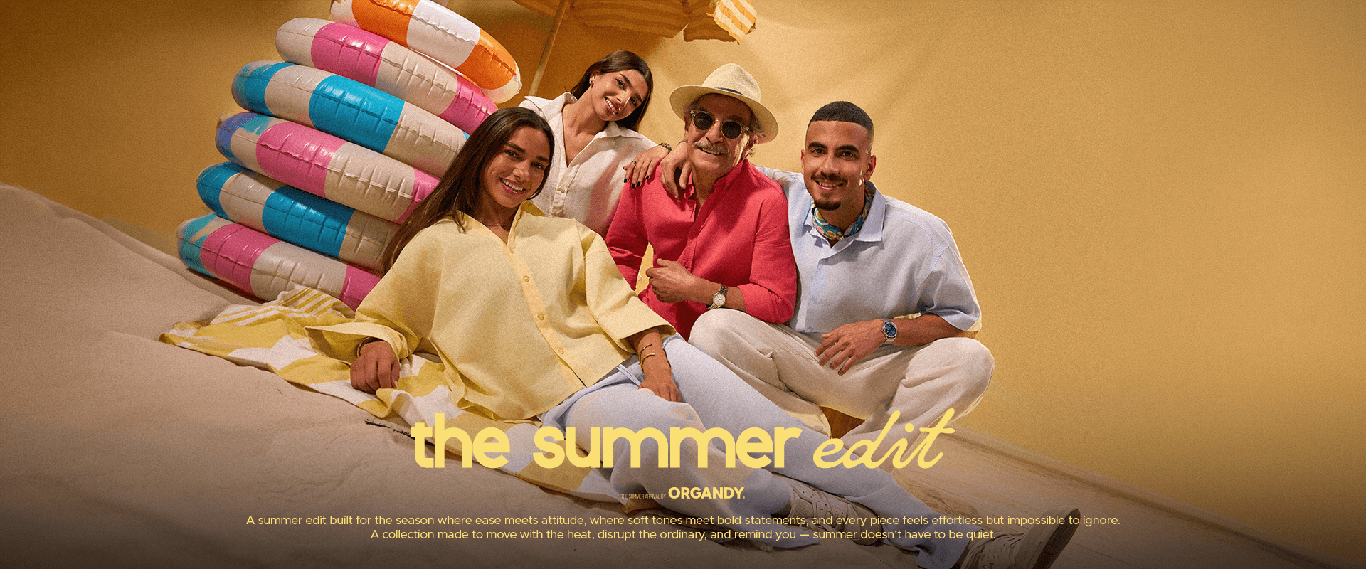 Four people sitting on a couch with colorful beach balls and an umbrella, posing for a photo against a yellow background.slider_item_zxRfHY